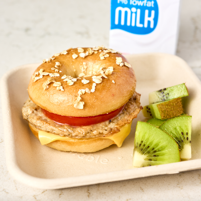 Breakfast bagel sandwich with a side of kiwi slices and a carton of milk in the background