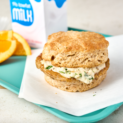 Biscuit and gravy sandwich on a blue tray, with orange slices and a carton of milk in the background