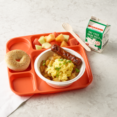 Breakfast bowl with a turkey sausage link, bagel, mixed fruit and a carton of milk on the side