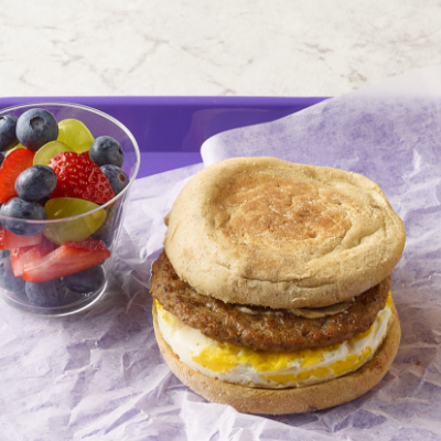 Maple butter turkey sausage breakfast sandwich with a cup of fruit on the side, on a purple tray