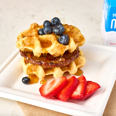 Sweet heat waffle sandwich topped with blueberries and sliced strawberries on the side