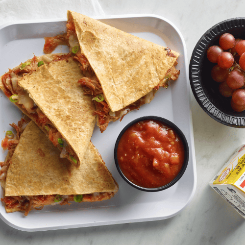 Korean BBQ turkey quesadilla on a lunch tray with a side of grapes